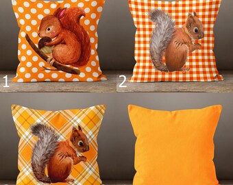 Könnte beinhalten: Vier dekorative Zierkissen. Das erste Kissen hat ein orangefarbenes Tupfenmuster mit einer Eichhörnchen-Illustration. Das zweite Kissen hat ein orange-weißes Karomuster mit einer Eichhörnchen-Illustration. Das dritte Kissen hat ein gelbes Karomuster mit einem Eichhörnchen. Das vierte Kissen ist einfarbig orange.