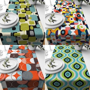 May include: Four table runners with vibrant geometric patterns are shown. The designs feature squares, circles, and abstract shapes in colours such as blue, green, orange, and yellow. Each runner is presented with white plates and decorative sprigs.