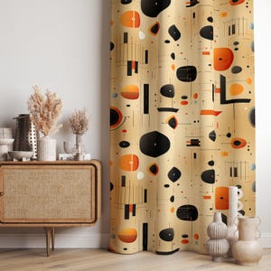 Puede incluir: Cortina beige con un diseño moderno de mediados de siglo. El patrón presenta formas geométricas negras, naranjas y blancas, incluyendo círculos, rectángulos y líneas. La cortina cuelga frente a una pared blanca y un mueble de madera.