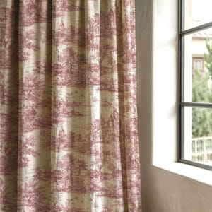 Op de afbeelding: Een gordijn met een herhalend toile de Jouy-patroon in crème- en bordeaux tinten. Het ontwerp toont een landschap met kastelen, bomen en figuren. Het gordijn hangt bij een raam.