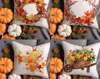 May include: Four decorative throw pillows with autumn-themed designs. Pillows feature watercolor illustrations of fall leaves, wreaths, and pumpkins. The pillows are surrounded by orange and white pumpkins and fall foliage.