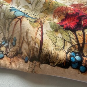 May include: Close-up of a fabric with a detailed botanical print. The design features large red and blue flowers, green leaves, and various plant elements. The color palette includes beige, brown, red, and blue tones, creating a vintage aesthetic.