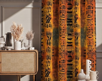 May include: A patterned curtain with a vibrant design in shades of orange, yellow, and black. The fabric features vertical stripes with abstract tribal-inspired motifs. The curtain is hanging in front of a neutral-colored wall.