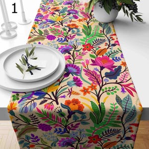 May include: A colorful floral table runner with a cream background. The runner features a variety of flowers and leaves in shades of pink, purple, orange, green, and blue.
