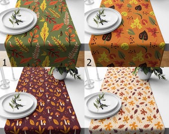May include: Four table runners with autumnal leaf and mushroom designs. The runners are in green, orange, burgundy, and beige. Each runner is displayed with white plates, cutlery, and a small plant.