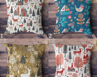 May include: Four square decorative throw pillows with holiday-themed designs. Pillows feature patterns of reindeer, trees, houses, and abstract shapes in various colors including white, teal, gold, and red. The pillows are displayed on a wooden surface.