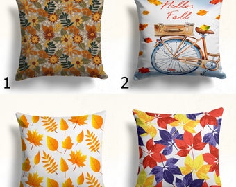 Könnte beinhalten: Vier dekorative Kissen mit herbstlichen Designs. Ein Kissen zeigt ein Blumenmuster in Braun-, Orange- und Grüntönen. Ein anderes zeigt ein Fahrrad mit einem Koffer und dem Text "Hello, Fall". Die anderen beiden Kissen haben Blättermuster.