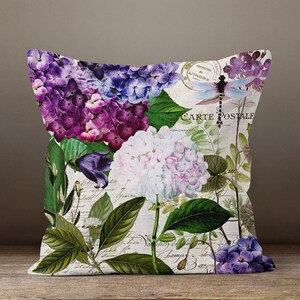 May include: Decorative throw pillow featuring a floral design with purple, white, and blue hydrangeas. The pillow has a vintage postcard theme with a dragonfly and script text.