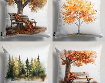 Puede incluir: Cuatro cojines cuadrados blancos con escenas otoñales en acuarela. Los diseños incluyen un árbol con un banco y una manta, un árbol con hojas naranjas y una escena de bosque.