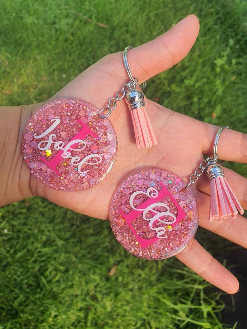 May include: Two pink glitter resin keyrings with silver key rings and pink tassels. One keyring says "Isabel" and the other says "Ella".