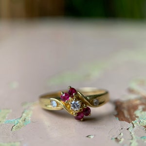 Può includere: Un anello d'oro con un solo diamante e un gruppo di rubini rossi incastonati in una fascia attorcigliata.