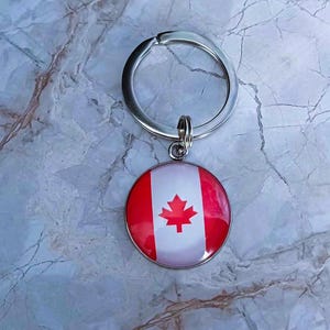 May include: A silver key ring with a round, red, white and red Canadian flag charm.