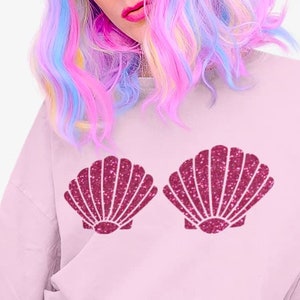Könnte beinhalten: Rosafarbener Pullover mit einem glitzernden rosa Muschel-Design auf der Vorderseite.