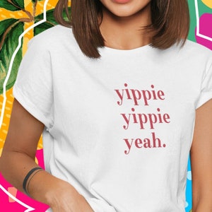 Könnte beinhalten: Weißes T-Shirt mit dem Text "yippie yippie yeah." in Rot gedruckt.
