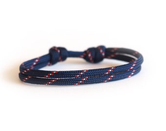 Può includere: Un braccialetto in corda blu navy con dettagli rossi e bianchi. Il braccialetto è annodato alle due estremità e presenta un design a doppio filo. Questo accessorio in stile nautico è adatto all'uso quotidiano.
