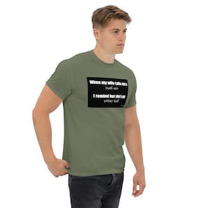 May include: Olive green t-shirt with the text "When my wife calls me a half-wit, I remind her she's my other half" in a black rectangle. The shirt is a solid color and has short sleeves.