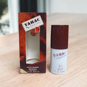 May include: A bottle of Tabac Original Eau de Cologne with a brown cap and white label, next to its matching box. The box is brown with the Tabac Original logo and text. The cologne bottle is 30 ml.