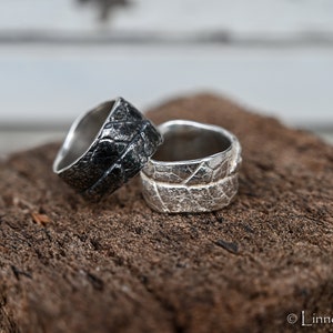 May include: Two silver rings with textured surfaces. One ring is oxidised black and the other is a natural silver colour.