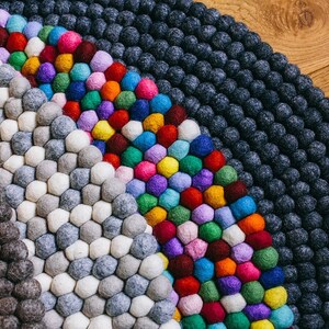 May include: A colorful, round felt ball rug. The rug features a variety of colors, including gray, white, blue, green, red, yellow, purple, and pink. The rug is made of small, round felt balls arranged in a pattern.
