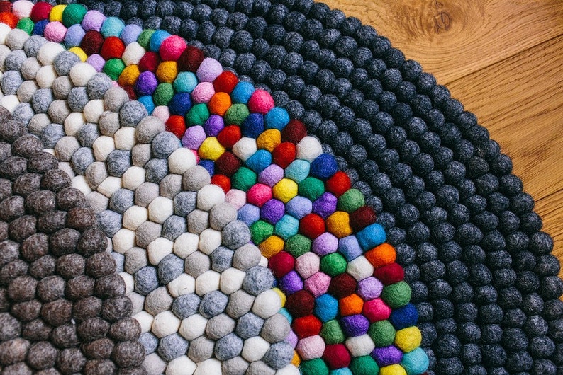 May include: A colorful, round felt ball rug. The rug features a variety of colors, including gray, white, blue, green, red, yellow, purple, and pink. The rug is made of small, round felt balls arranged in a pattern.