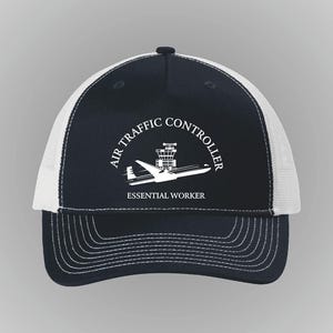 Pode incluir: Boné de caminhoneiro azul marinho e branco com o texto "AIR TRAFFIC CONTROLLER" em semicírculo acima de uma ilustração de um avião e torre de controle. O texto "ESSENTIAL WORKER" está abaixo. Com aba curva.