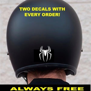 May include: Black motorcycle helmet with a white spider decal on the back. The helmet has the text "TWO DECALS WITH EVERY ORDER!" and "ALWAYS FREE SHIPPING!" printed on it.