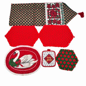 May include: A collection of Christmas-themed kitchen textiles. Includes a green and gold patterned table runner, two red crocheted hot pads, a red and white swan placemat, a square pot holder with a reindeer design, and a green and red crocheted hot pad.