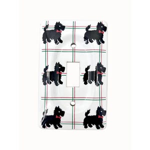 May include: White light switch cover featuring a repeating pattern of black Scottish Terrier dogs with red bow ties. The background has a plaid design with red and green lines. The switch cover has a rectangular opening for the switch.