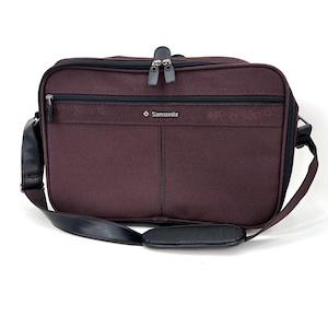 May include: A burgundy Samsonite briefcase with a black shoulder strap and handle. The bag has a zippered front pocket and a main compartment with a double zipper closure. The Samsonite logo is visible on the front.