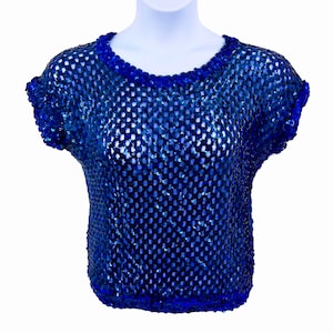 May include: A blue sequined top with a round neckline and short sleeves. The top is made of a mesh material and is covered in small, shiny sequins. The neckline and sleeve edges are trimmed with a darker blue fabric.