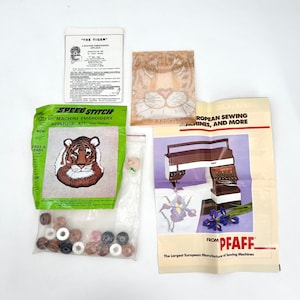 May include: A collection of sewing and embroidery supplies, including a "SPEED STITCH" applique kit with a tiger design, a "THE TIGER" instruction sheet, and a brochure from PFAFF. Also included are beads and a tiger face applique.
