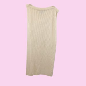 May include: A cream-colored, ribbed knit tube top. The top is sleeveless and has a straight neckline. The fabric has vertical ribbing, creating a textured appearance. The background is a solid light pink.