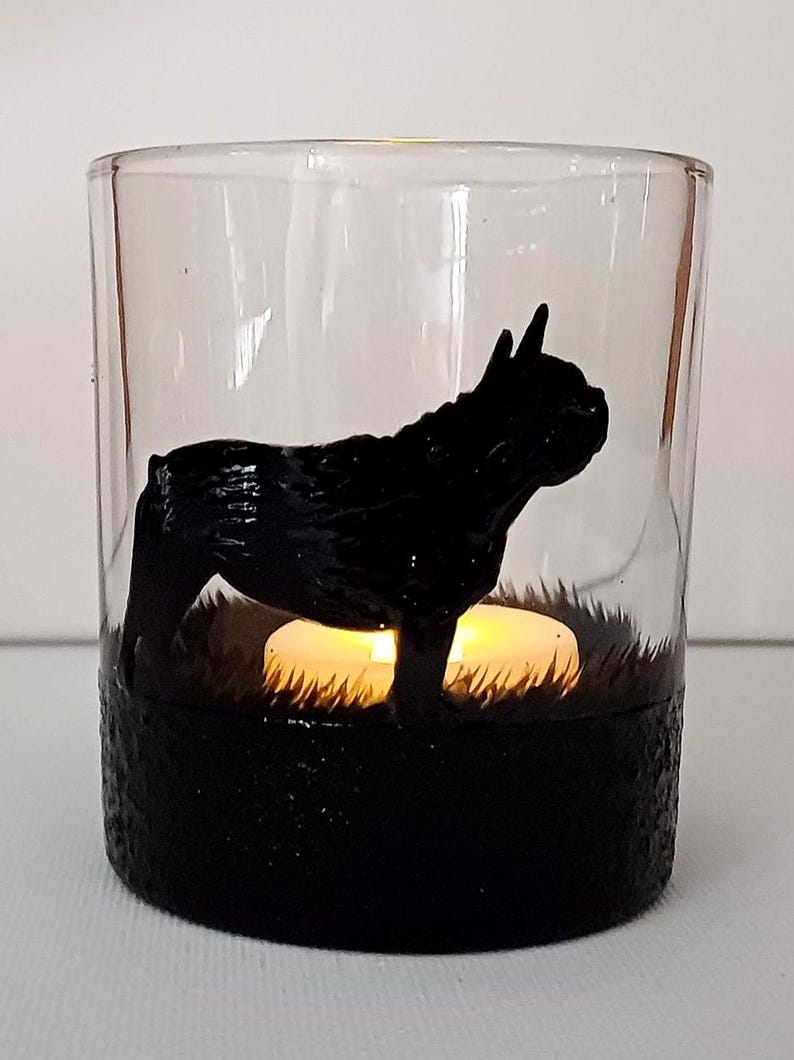 May include: A glass candle holder with a black silhouette of a French Bulldog. The holder has a black base and a clear glass top. A small white candle is inside the holder.