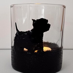 May include: A glass candle holder with a black silhouette of a dog sitting on a black textured base. The candle holder is lit with a small candle inside.