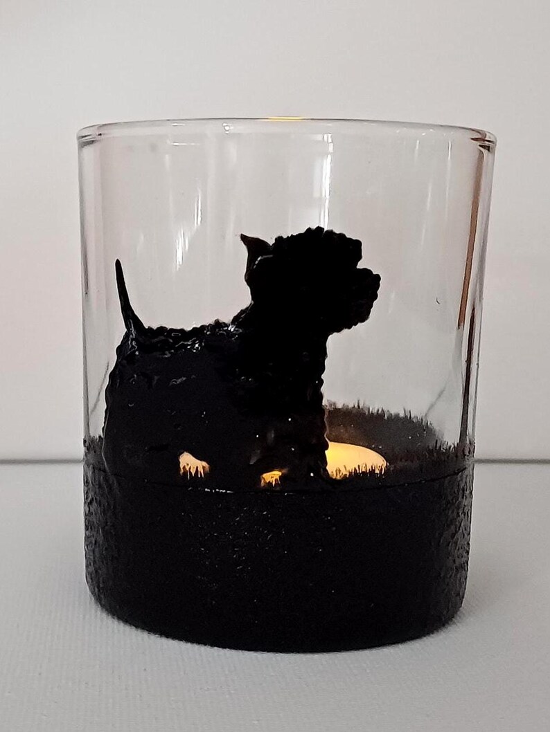 May include: A glass candle holder with a black silhouette of a dog sitting on a black textured base. The candle holder is lit with a small candle inside.