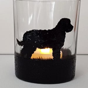 May include: A glass candle holder with a black silhouette of a dog. The candle holder has a black base and a clear glass top. The silhouette of the dog is painted on the glass.