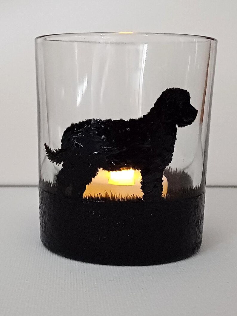 May include: A glass candle holder with a black silhouette of a dog. The candle holder has a black base and a clear glass top. The silhouette of the dog is painted on the glass.