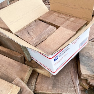 May include: A cardboard box filled with various pieces of wood, labeled "Priority Mail" and "Large Flat Rate Box". The box is open and the wood is spilling out.