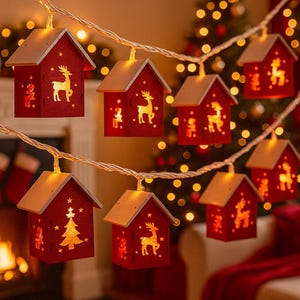 May include: A festive string of red, house-shaped fairy lights, each with a warm white glow. The houses feature gold-coloured cut-out designs of reindeer and Christmas trees. The lights are strung on a thin, clear wire, perfect for Christmas.