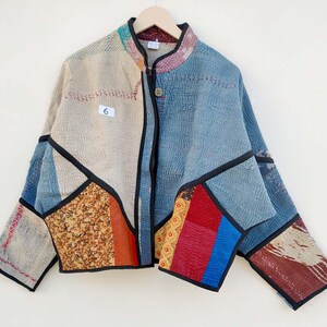 May include: A long-sleeve jacket constructed from various quilted fabric patches in shades of blue, beige, red, and orange. The garment features a mandarin collar, a single button closure, and black piping along the seams. A white tag with the number 6 is attached to the front.