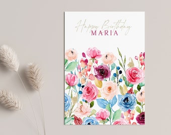 May include: A white card with the text "Happy Birthday MARIA" in gold script. The card is decorated with a watercolor floral border of pink, blue, and purple flowers.