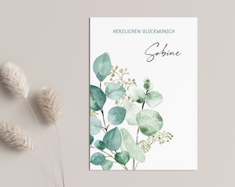 May include: A white card with the text "Herzlichen Glückwunsch Sabine" and a watercolor illustration of green eucalyptus leaves.