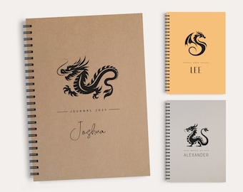 May include: Spiral-bound journals with dragon designs. The largest journal is tan with a black dragon illustration, the text "JOURNAL 2024" and the name "Joshua". Two smaller journals are also shown, one orange and one gray, each with a dragon logo.