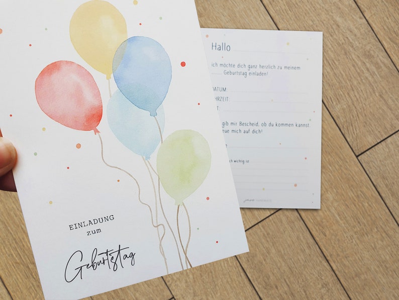 May include: A white card with a watercolor illustration of colorful balloons and the text "EINLADUNG zum Geburtstag". The card is on a wooden surface. The text "Hallo" is on a separate white card with the text "ich m&ouml;chte dich ganz herzlich zu meinem Geburtstag einladen!" and blank lines for the date, time, and a message.