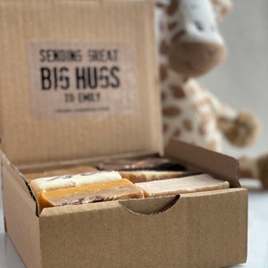Op de afbeelding: Een bruine kartonnen doos met de tekst "Sending Great Big Hugs To Emily" op de voorkant. De doos is open en bevat verschillende repen fudge in verschillende smaken.