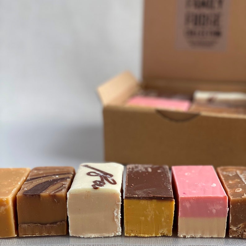 Op de afbeelding: Assortiment van zes verschillende smaken fudge-repen in een kartonnen doos. De smaken zijn onder andere witte chocolade, chocolade, vanille, aardbei en twee andere smaken.