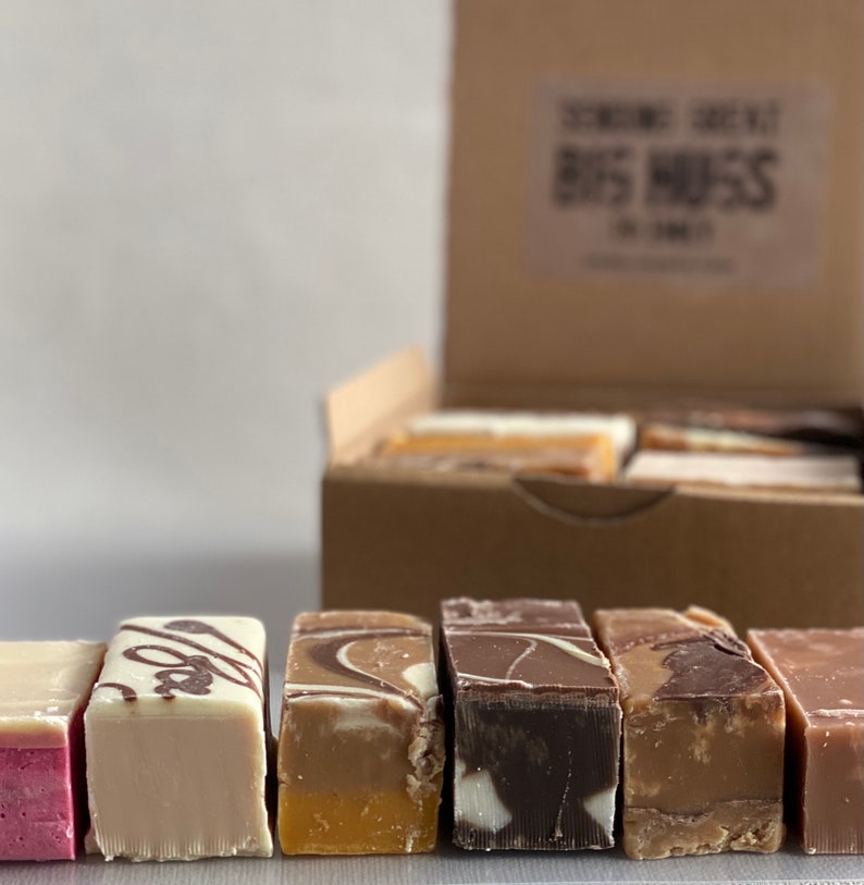 Op de afbeelding: Een doos met verschillende fudge-soorten met smaken zoals chocolade, vanille en karamel. De doos is gelabeld met "Scrumptious Scrummy Big Mess".