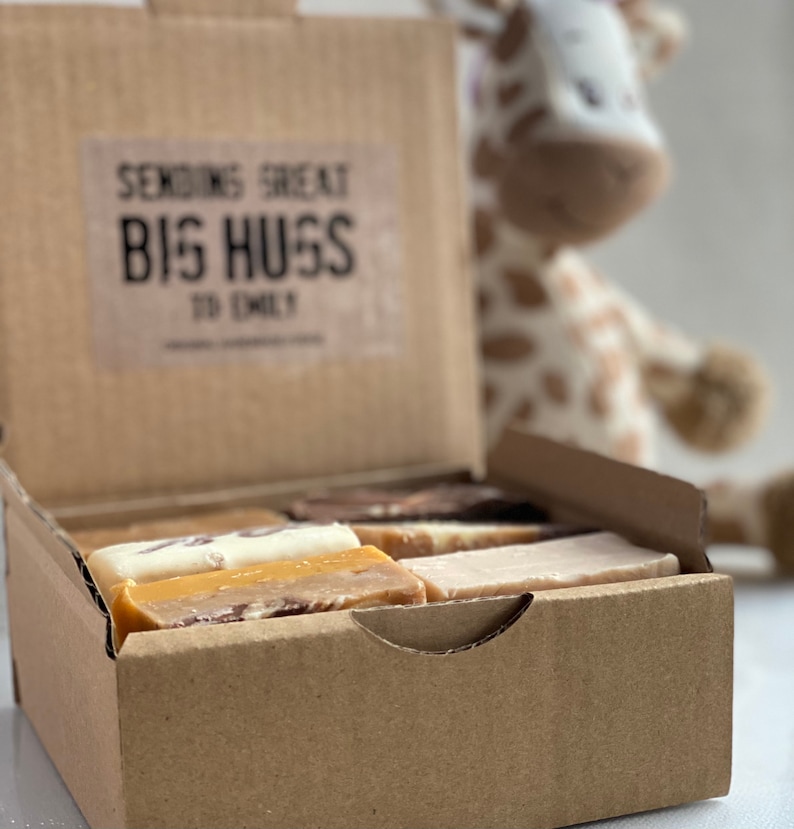 Op de afbeelding: Een bruine kartonnen doos met de tekst "Sending Great Big Hugs To Emily" op de voorkant. De doos is open en bevat verschillende repen fudge in verschillende smaken.
