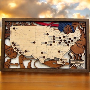 May include: A wooden map of the United States with baseball-themed details. The map is framed in dark wood and features a baseball glove, bats, and a baseball. The map is decorated with small circles representing locations across the country. The text "CARRANZA FAMILY Baseball Tradition" is displayed at the bottom of the map.