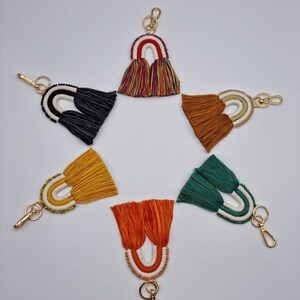 May include: Set of seven rainbow-coloured keychains with beaded accents and tassel fringe. Each keychain features a different colour combination of rainbow stripes.